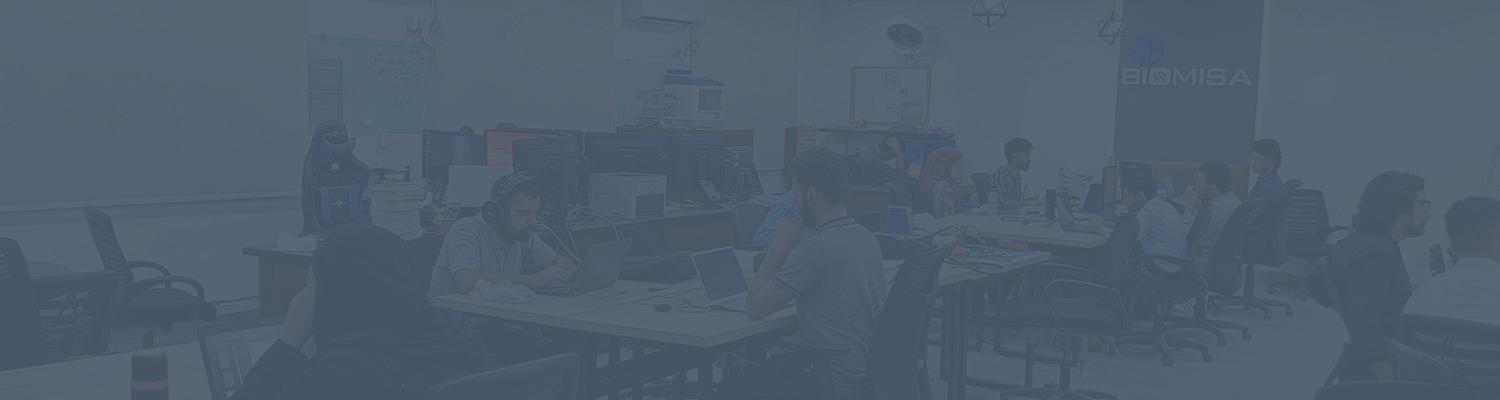 Office environment with multiple people working at desks with laptops, engaging in discussions, and collaborating in a workspace.